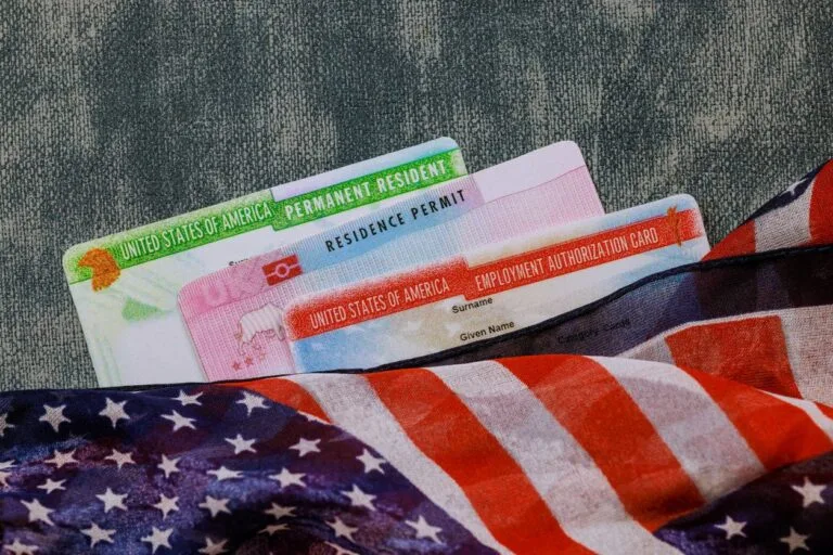 US green card, employment authorization card and residence permit card partially covered with an American flag